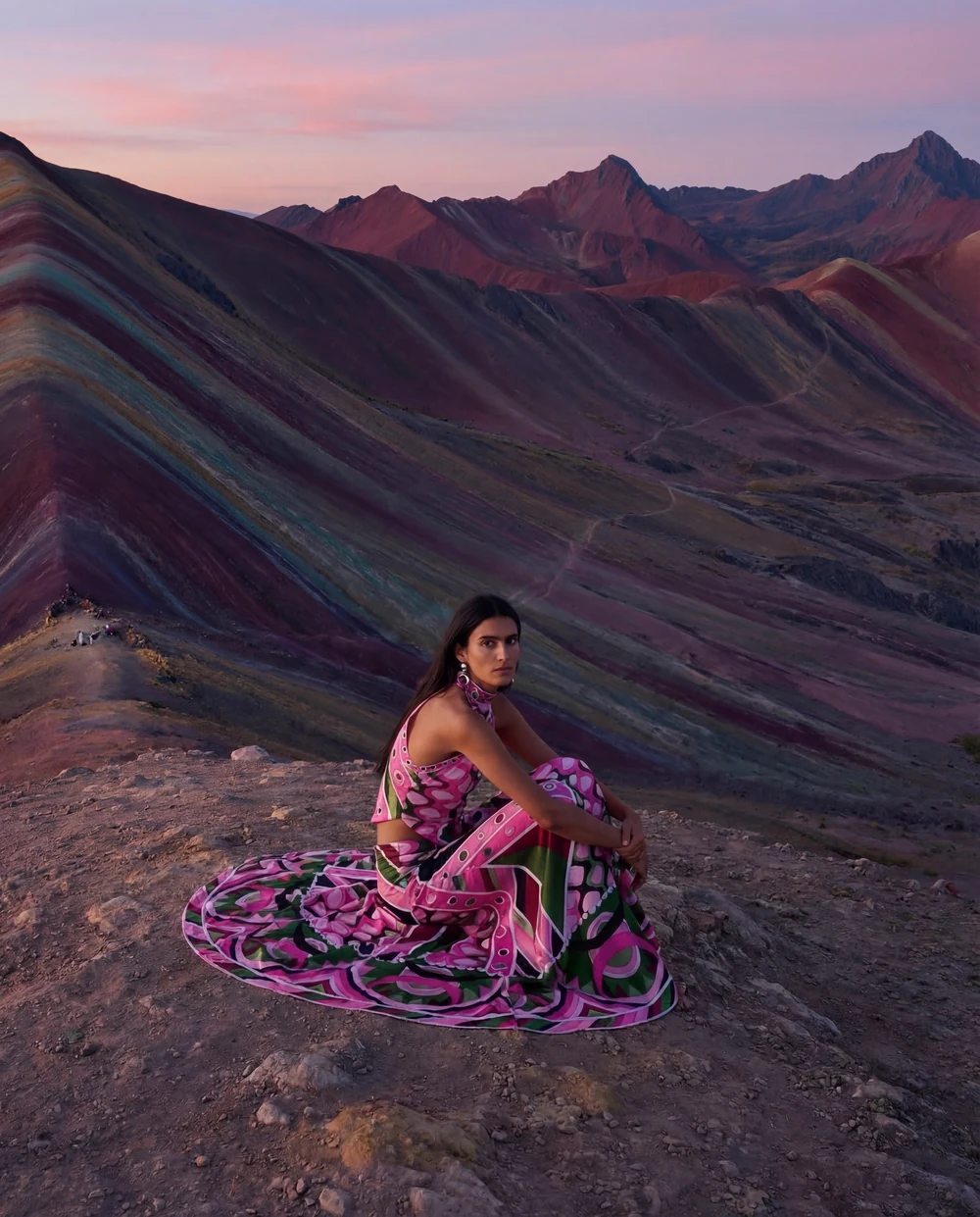 Woman in a flowing pink patterned dress against colourful mountain ridges