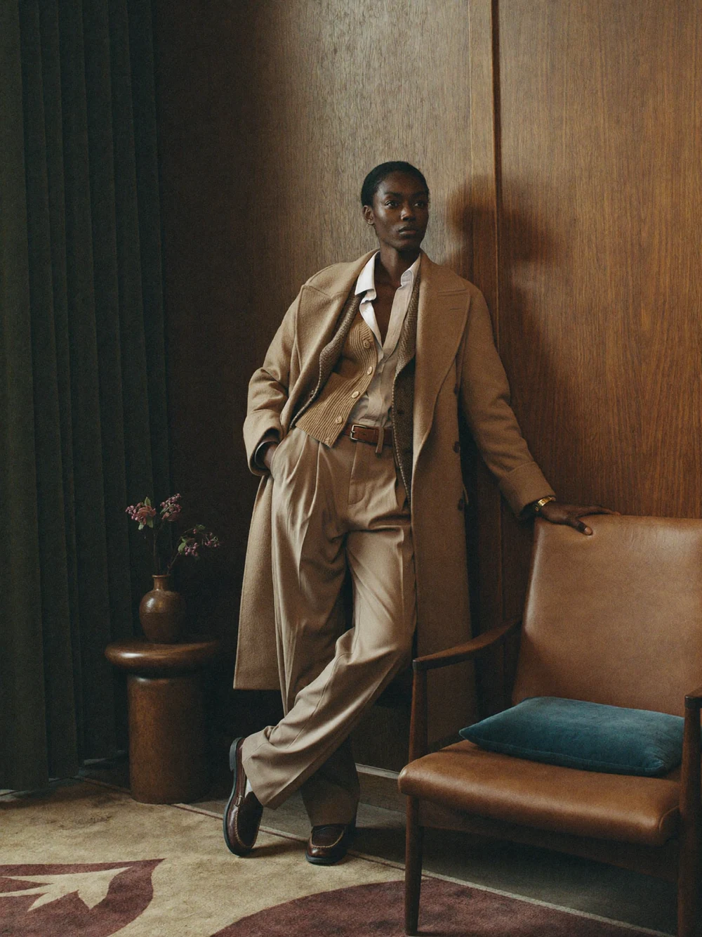 Man in a sand coloured suit standing in a warmly lit wood panelled room