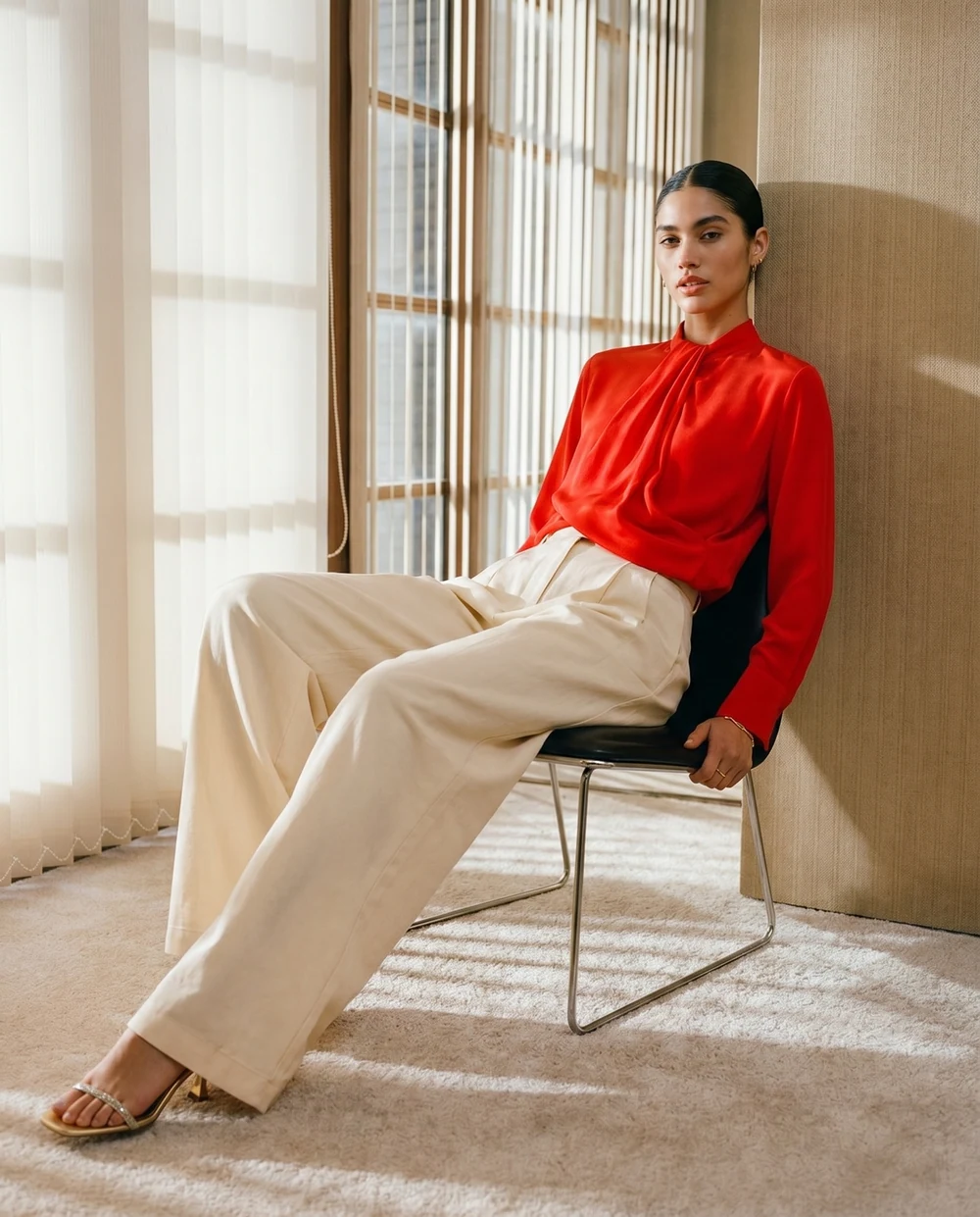 Woman in a vivid red blouse and cream trousers seated in a sunlit room