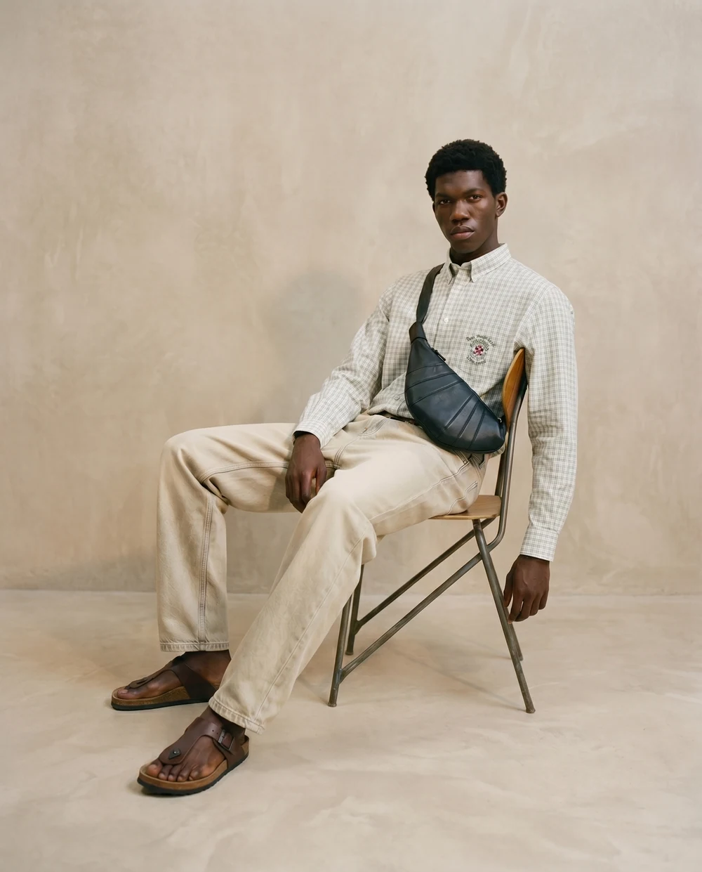 Man in a light suit and crossbody bag seated on a folding chair