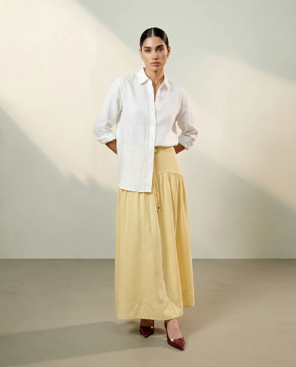 Woman in a white shirt and long yellow skirt against a pale studio background