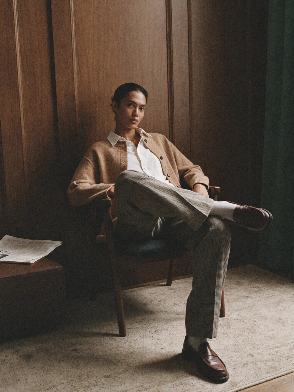 Man in a tan jacket seated in a dark wood panelled room